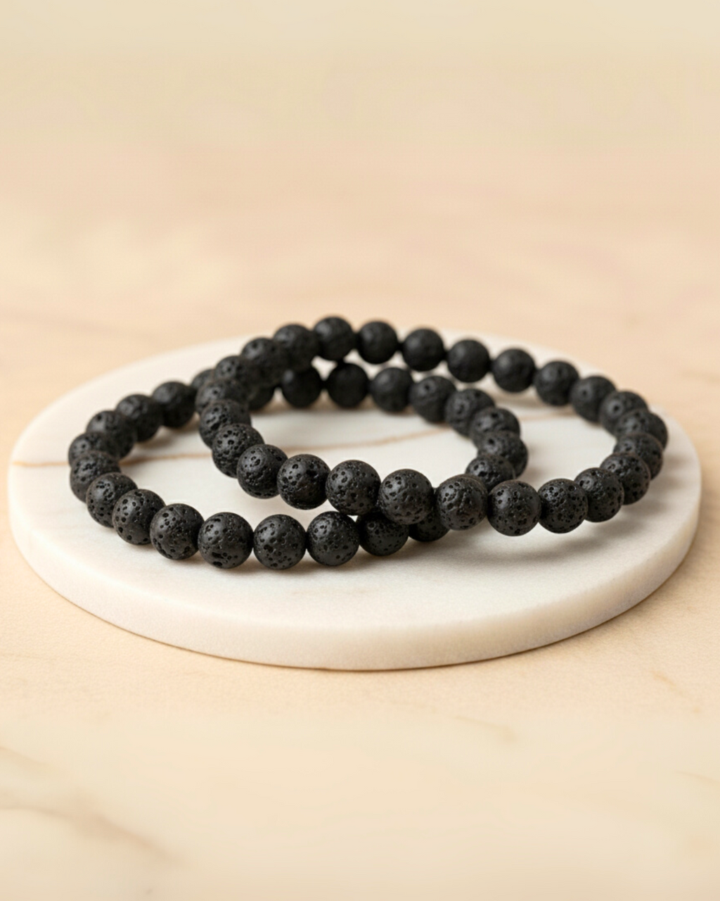 Black beaded lava bracelets on a white circular stone surface with a beige background