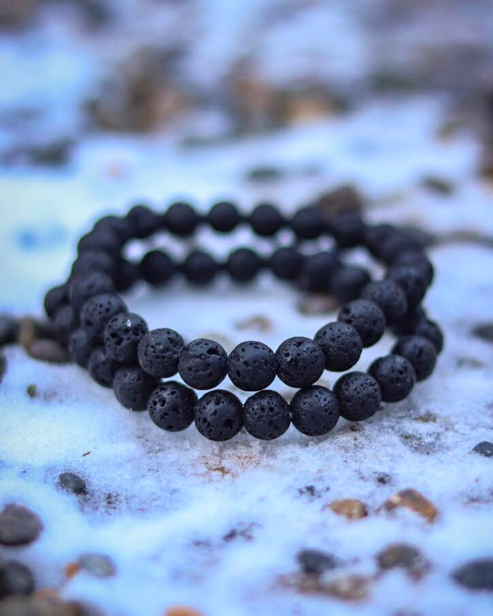 Two black lava stone bracelets on a snowy ground