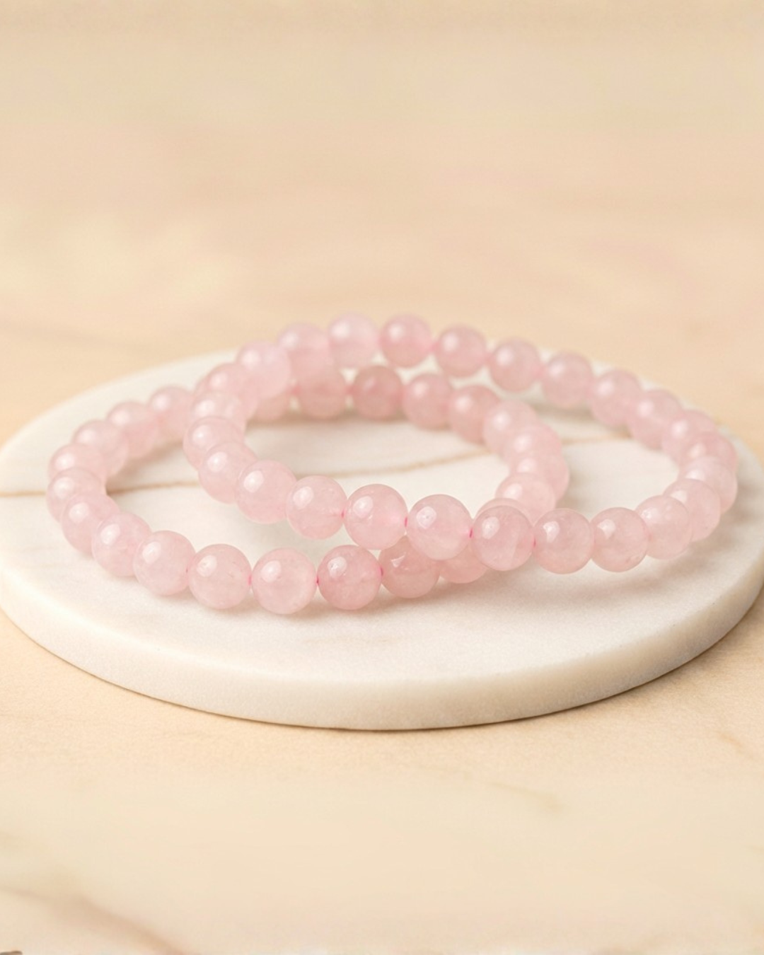 Two pink beaded Rose Quartz bracelets on a white circular base with a beige background