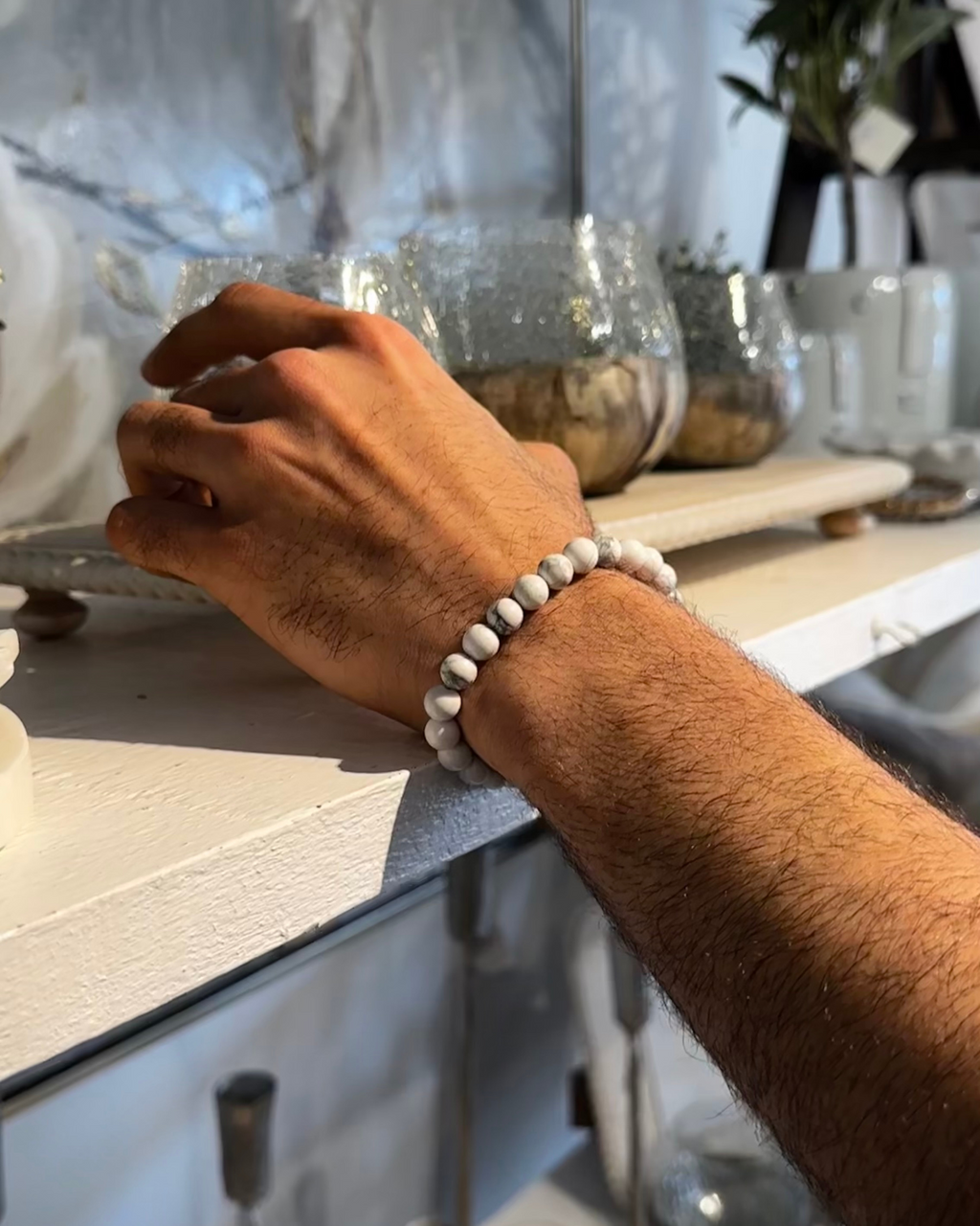 Hand with a beaded Howlite Bracelet on a countertop with jars in the background