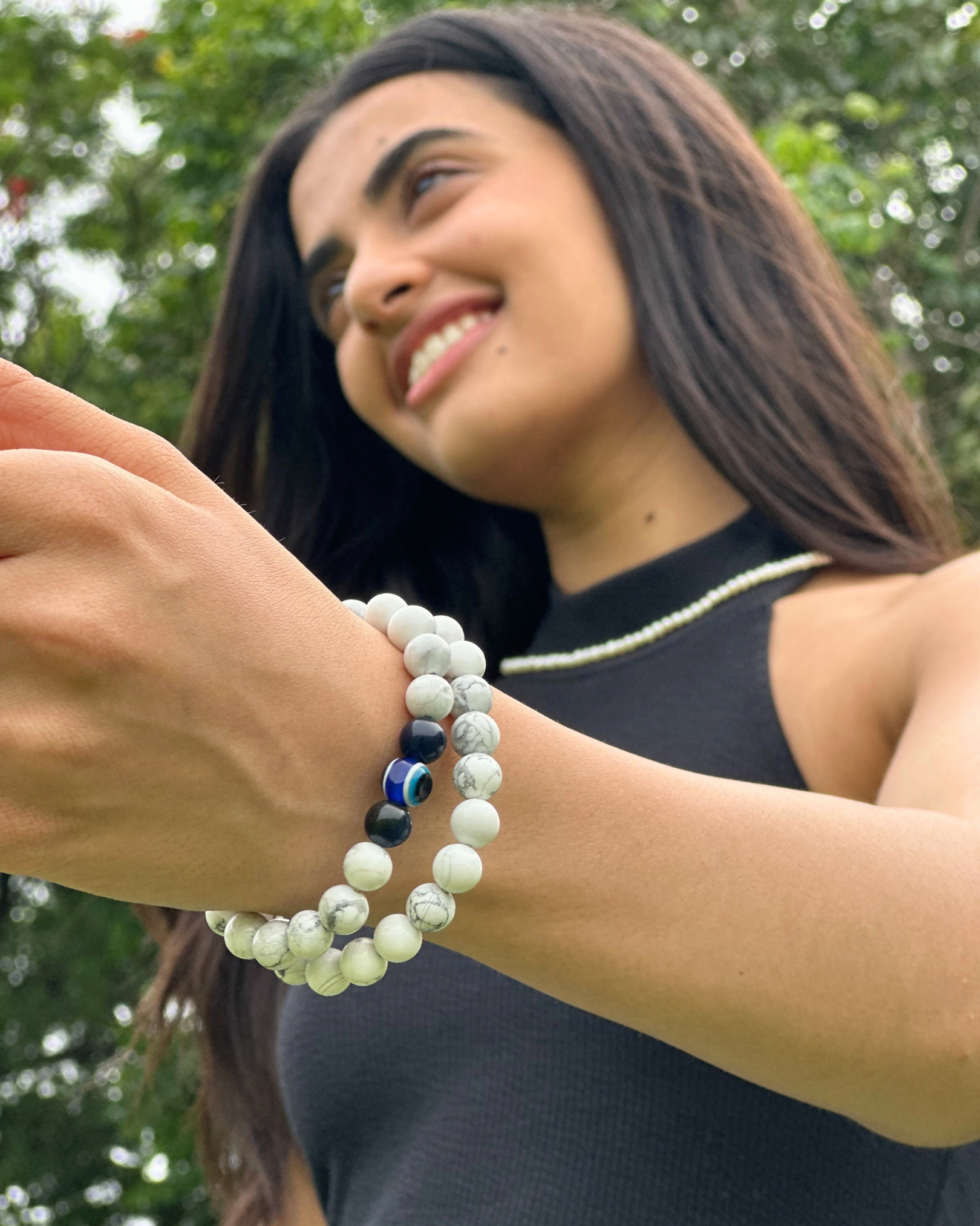 Woman wearing multiple Howlite Bracelet on her wrist with a blurred green background